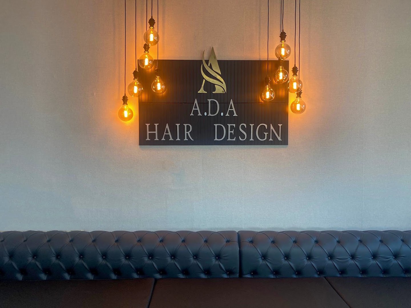 Het interieur van A.D.A Hair Design: het logo-bord met Edison-gloeilampen boven een leren chesterfield-bank